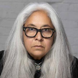 Portrait photo of Laurie Steelink. Steelink has long, straight gray hair and wears a black top and black-rimmed glasses.